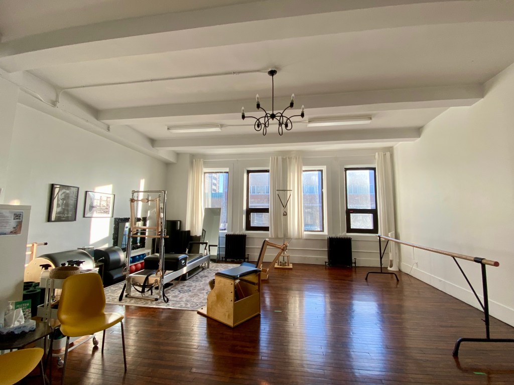 Bright Pilates studio interior with private equipment space and small group area, filled with natural light from large windows.